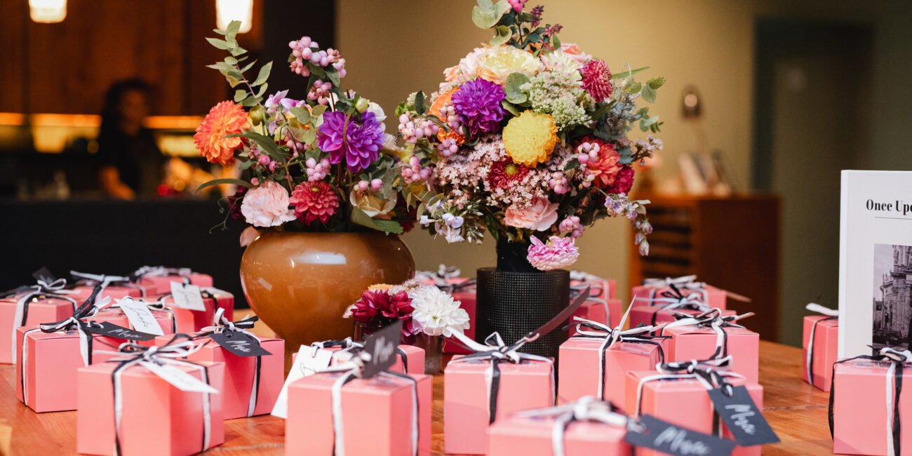 Einzeln verpackte Gastgeschenke in rosafarbenen Kartons auf einem Tisch mit zwei Blumenvasen