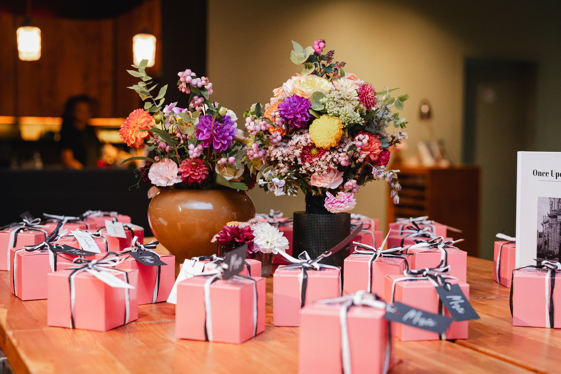 Einzeln verpackte Gastgeschenke in rosafarbenen Kartons auf einem Tisch mit zwei Blumenvasen